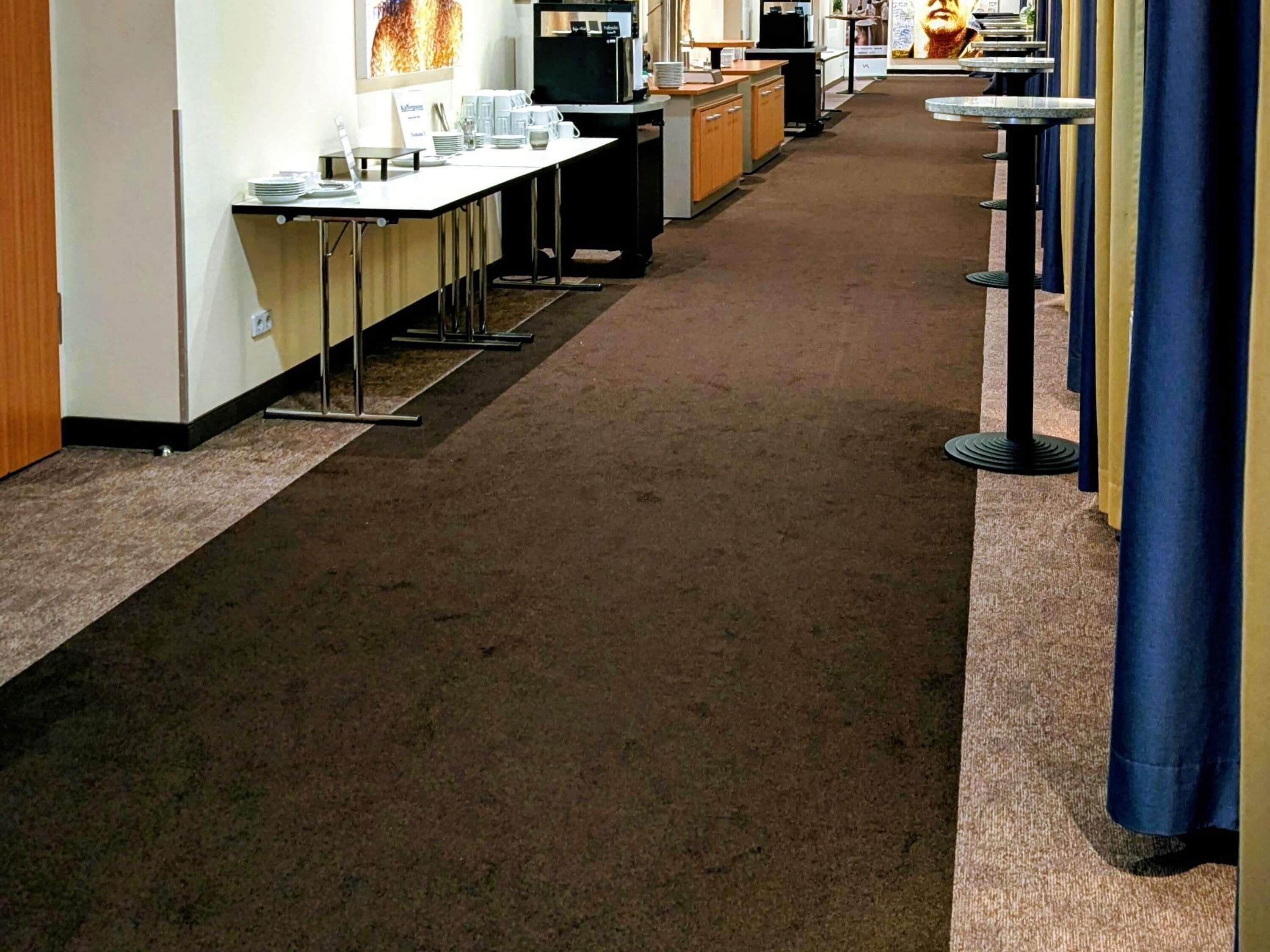 Un pasillo de hotel con un mostrador de recepción alargado, una máquina de café y un mostrador con un menú.