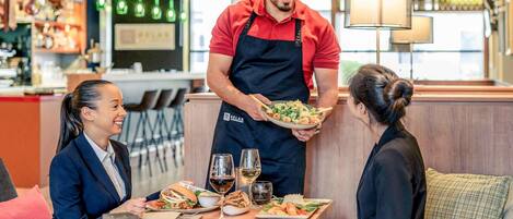 A restaurant setting with a waiter serving food to two customers.