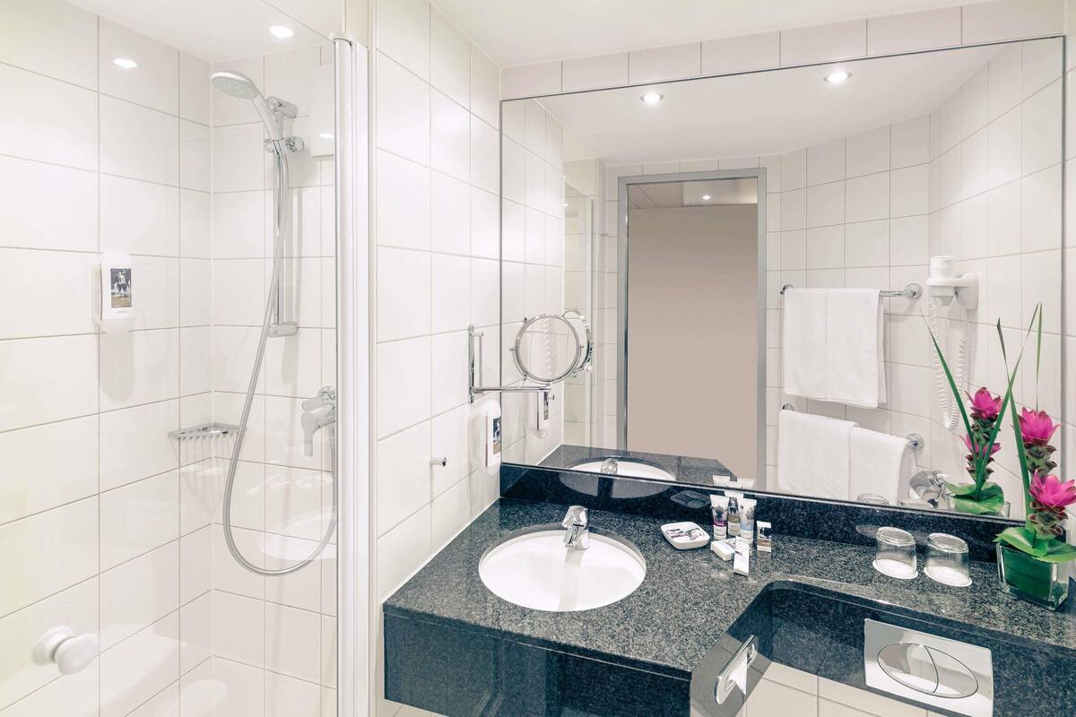 A modern bathroom with a glass-enclosed shower, a sink with a dark countertop, and a large mirror.