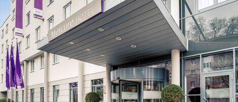 Una entrada de hotel moderna con porche cubierto, puertas de cristal y un cartel que dice "Mercure Hotel".