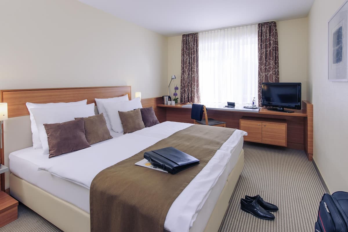 Una habitación de hotel con cama, escritorio, televisor y maleta.