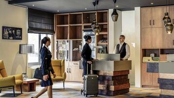 A hotel lobby with a reception desk, seating area, and a large window.