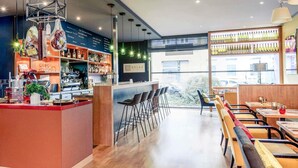Un espace bar moderne avec un comptoir en bois, des luminaires suspendus et une vue sur la rue.
