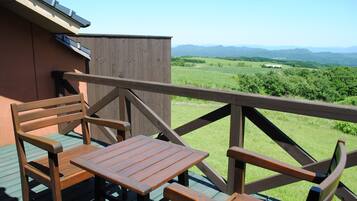 A wooden deck with a table and chairs, overlooking a green landscape with distant mountains.
