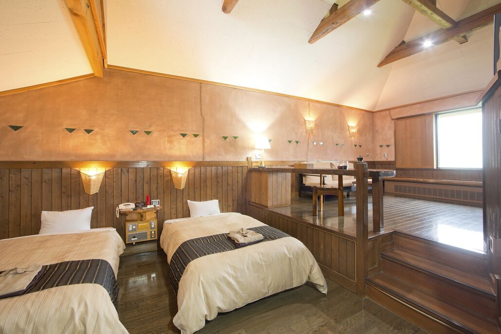 Quarto com paredes de madeira, uma cama, uma mesa de cabeceira, uma luminária e uma janela.