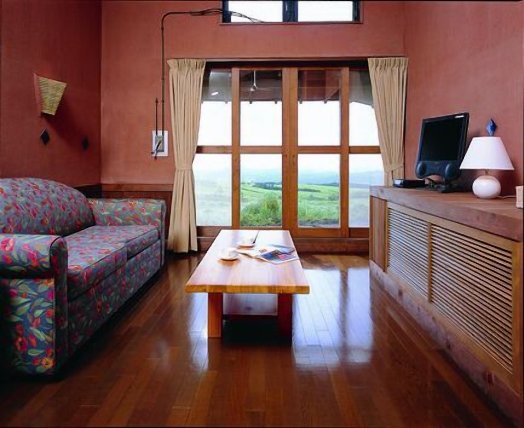Quarto com sofá, mesa, televisão e janela com cortinas.