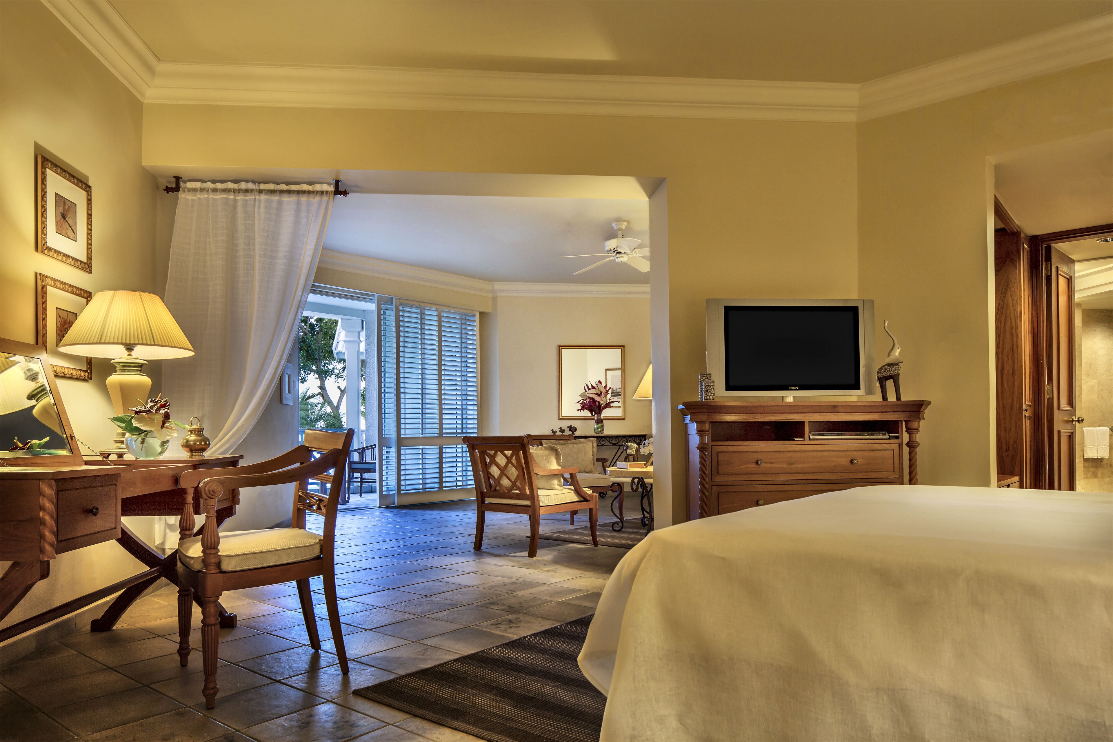 A hotel room with a bed, a desk with a lamp, a chair, a television, and a view of the outdoors through a window.