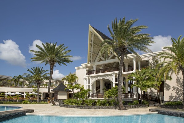 A resort with a pool, palm trees, and a large building with a balcony. - The Residence Mauritius (Belle Mare)