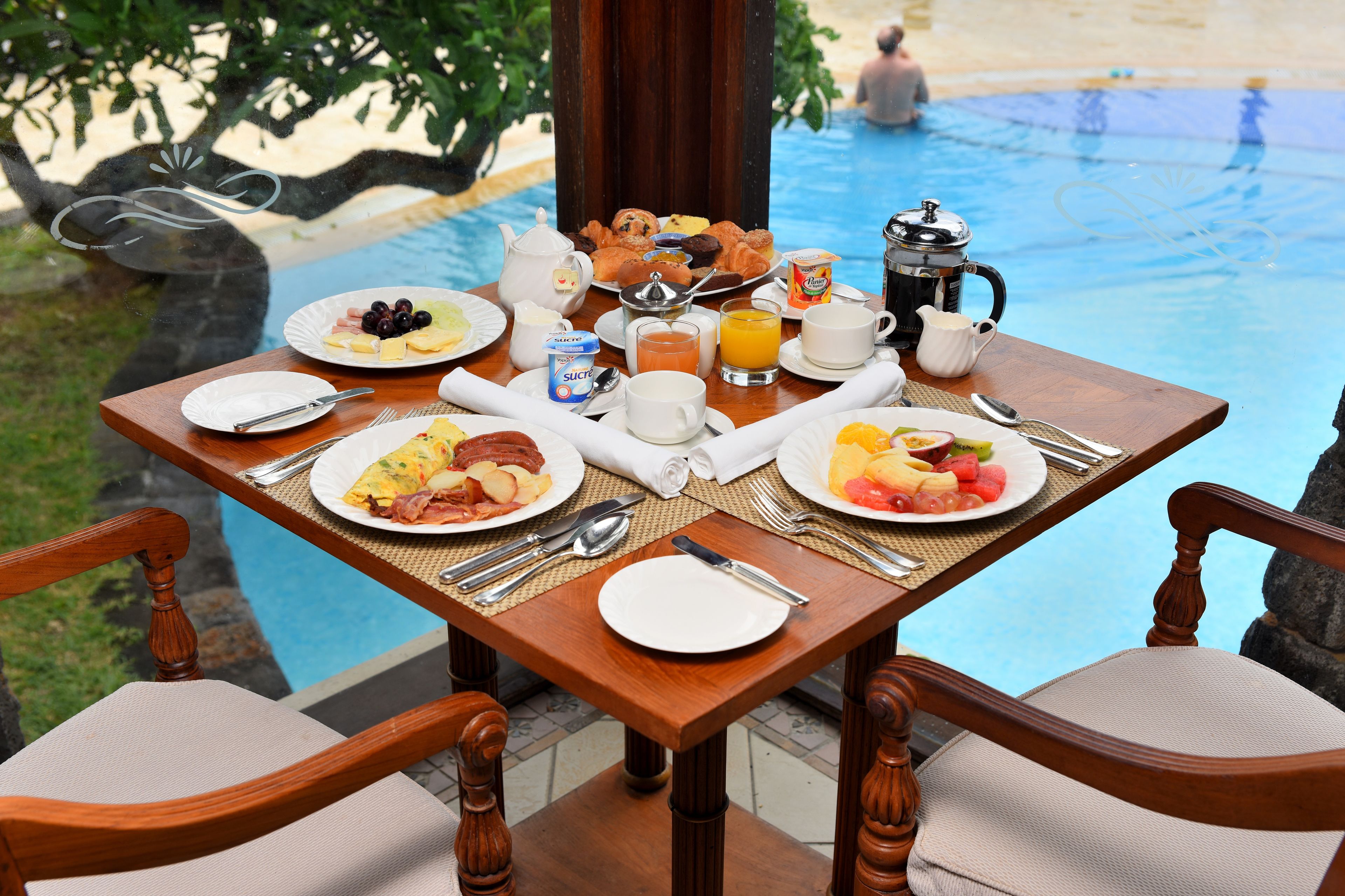 Une table de petit-déjeuner avec des assiettes remplies de nourriture, une cafetière et une vue sur une piscine.