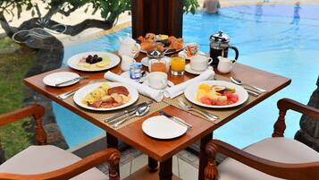 Une table de petit-déjeuner avec des assiettes remplies de nourriture, une cafetière et une vue sur une piscine.