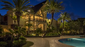 Un resort con piscina, palmeras y un edificio bien iluminado al anochecer.