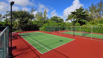 Una cancha de tenis con red, rodeada por una cerca y árboles.