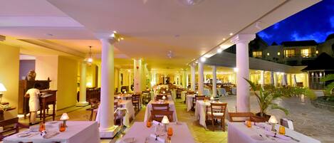 A restaurant with multiple tables and chairs, a ceiling fan, and a view of the outside at night.