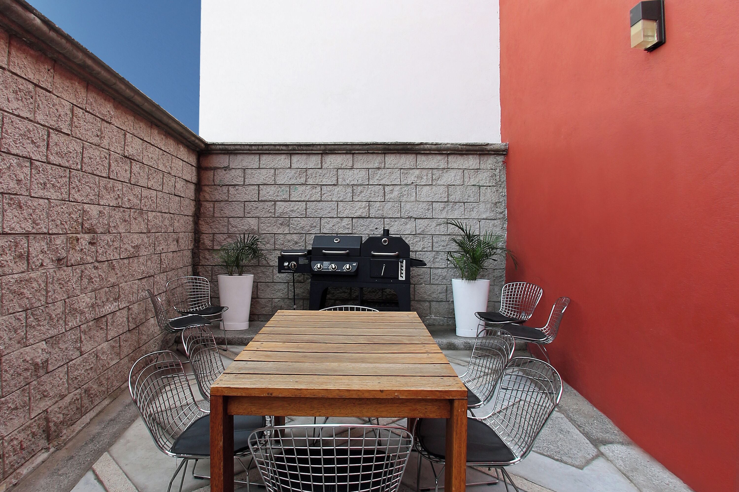 A patio with a wooden table and metal chairs, a barbecue grill, and potted plants.