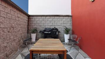 A patio with a wooden table and metal chairs, a barbecue grill, and potted plants.