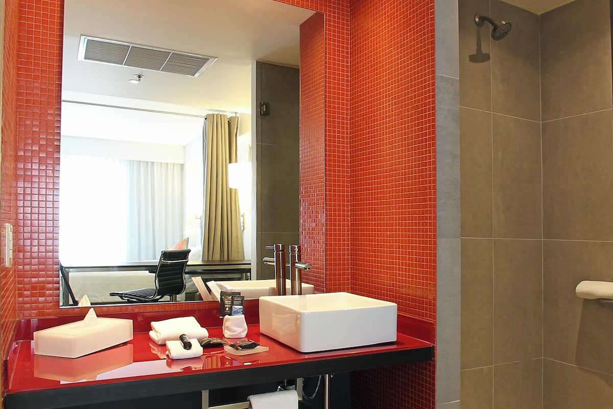 Un baño moderno con ducha de azulejos rojos, un lavamanos blanco y un espejo encima.