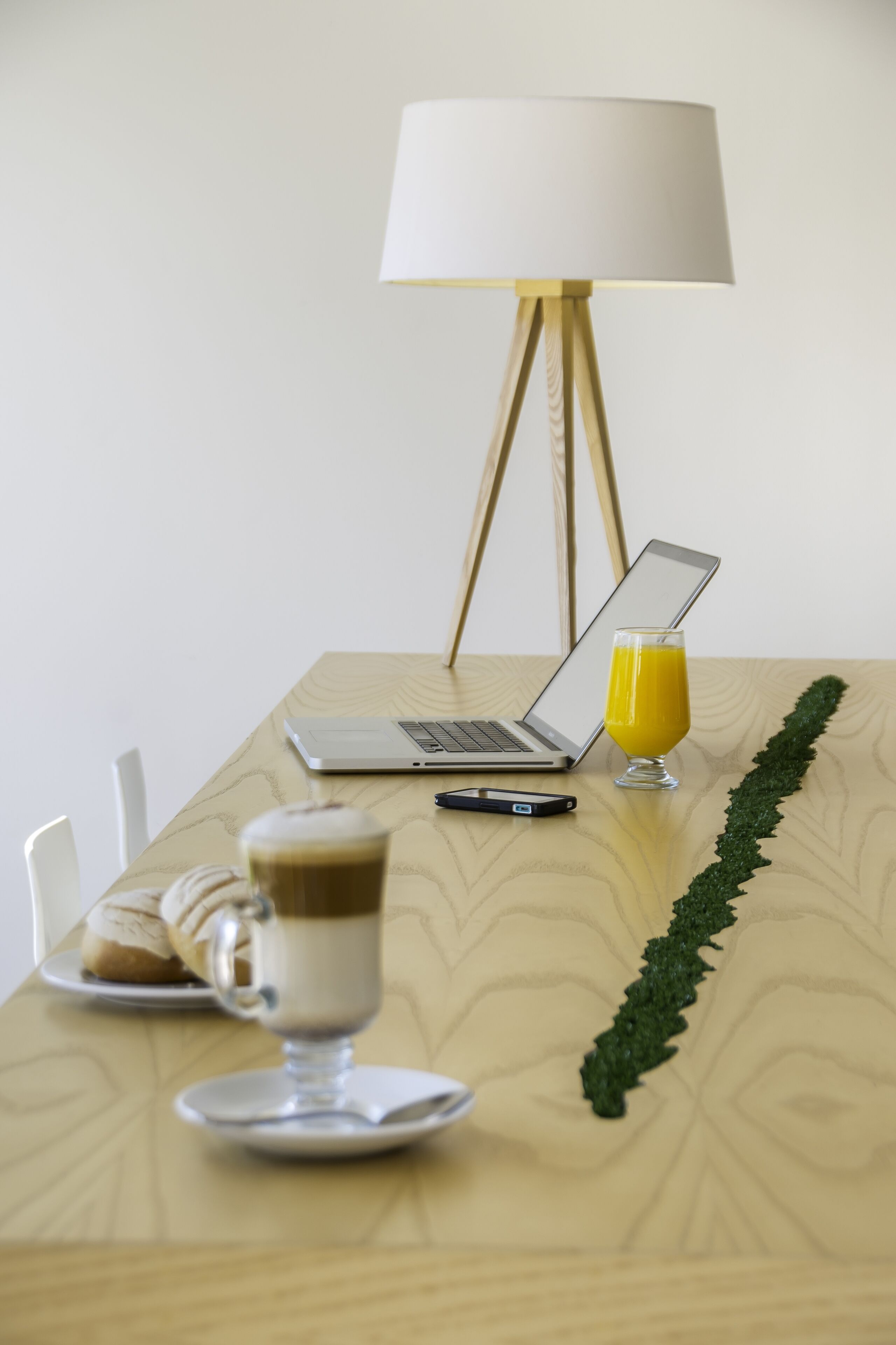 Una mesa de madera con una computadora portátil, un vaso de jugo de naranja, una taza de café y un pastel.