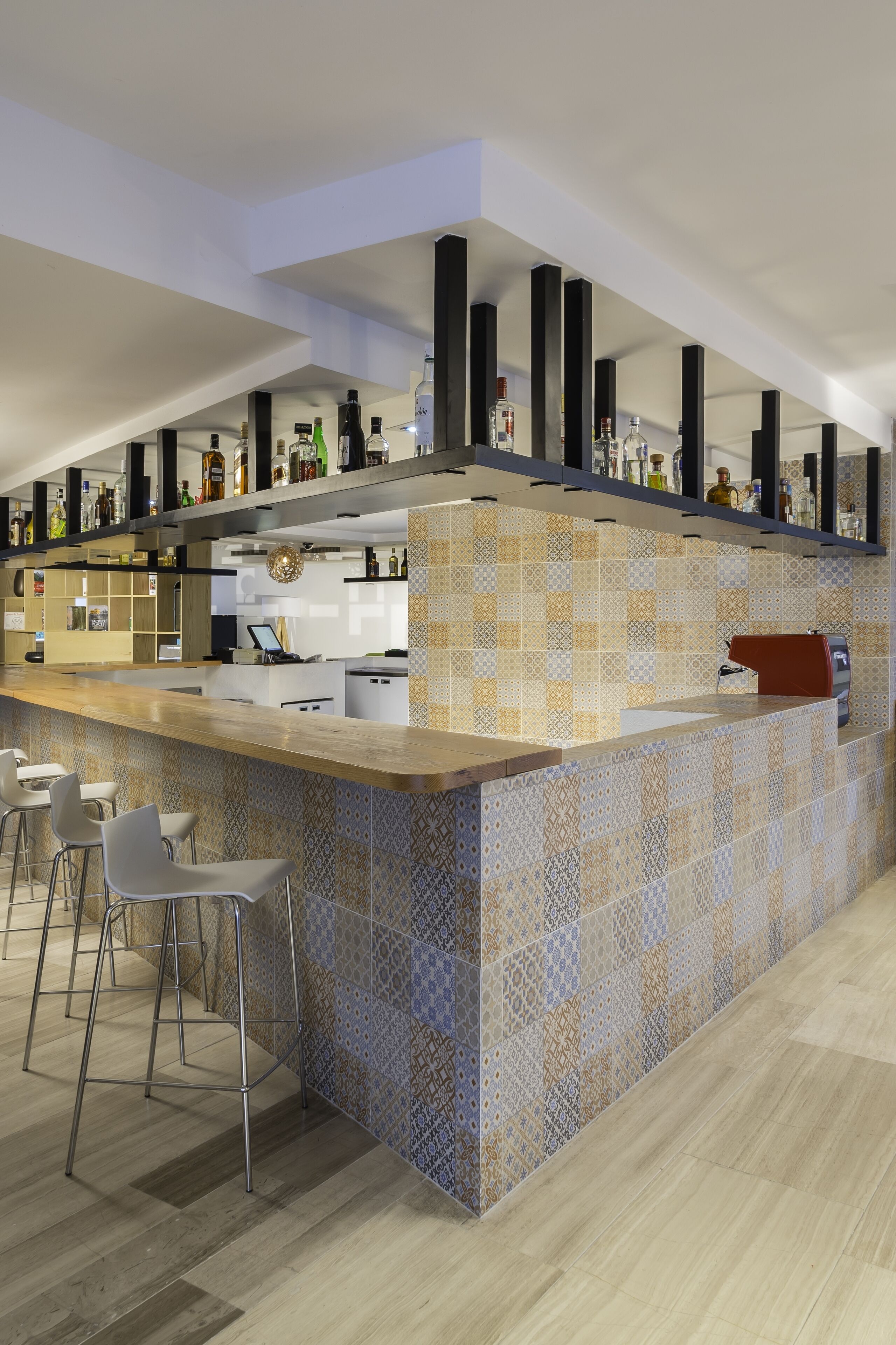 A modern bar area with a patterned tile backsplash, bar stools, and a variety of bottles on shelves.