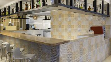 A modern bar area with a patterned tile backsplash, bar stools, and a variety of bottles on shelves.