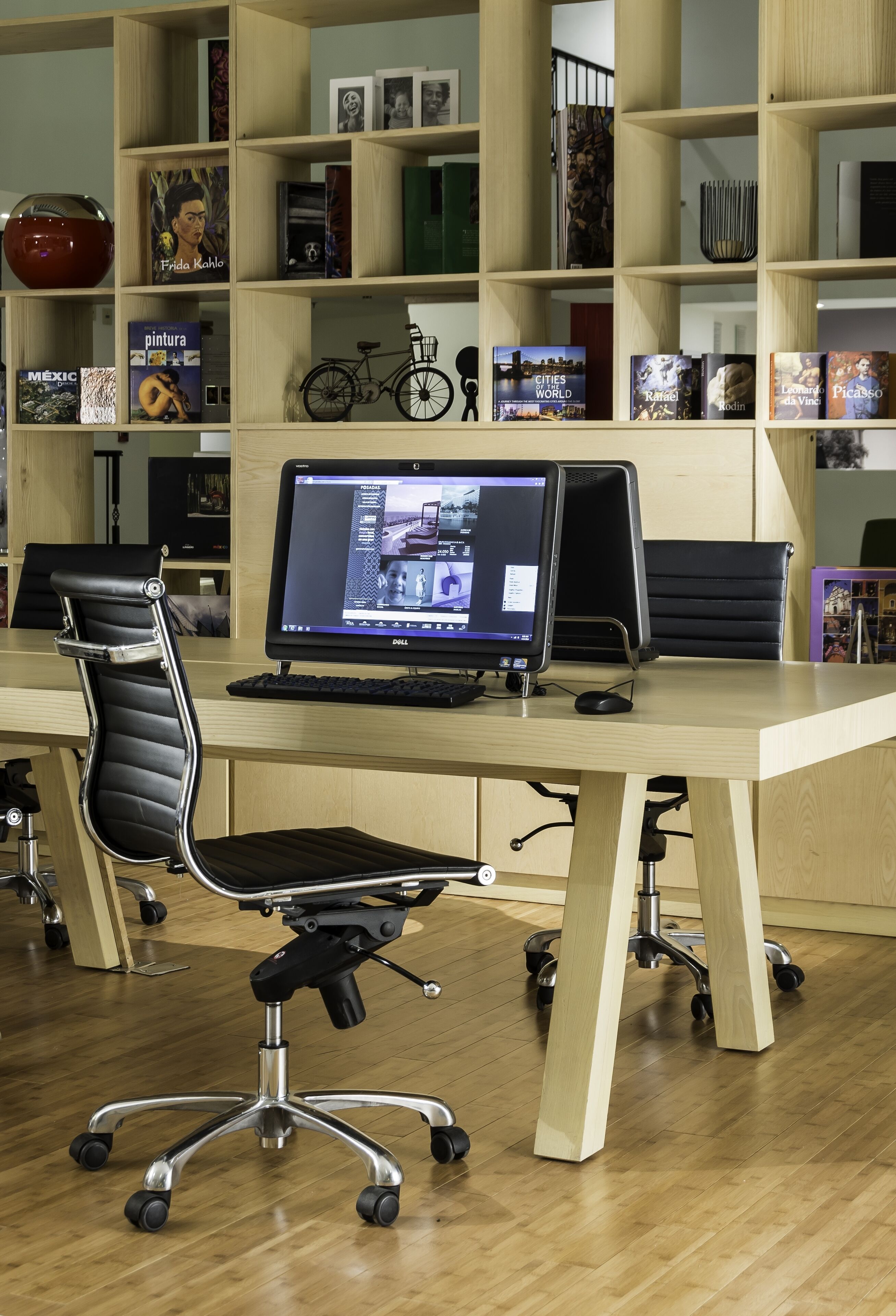 A modern office with a wooden desk, a black office chair, and a computer monitor displaying a webpage.