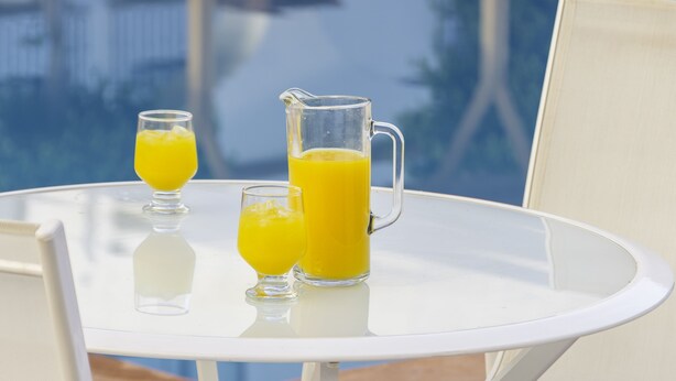 A table with a pitcher and two glasses of orange juice, set against a view of a pool and buildings. - Fiesta Inn Queretaro (Querétaro)
