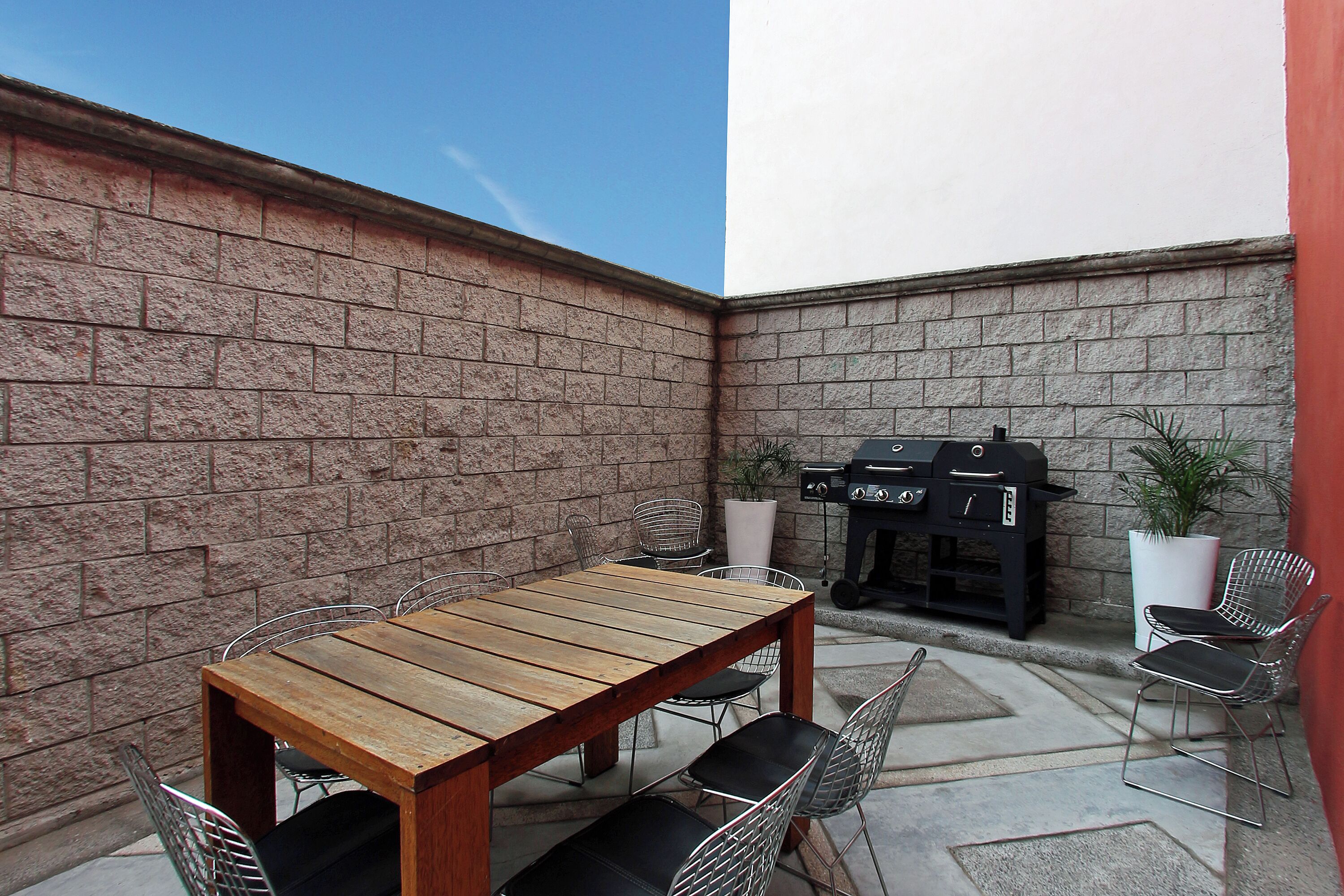 A patio area with a wooden table and metal chairs, a barbecue grill, and potted plants.