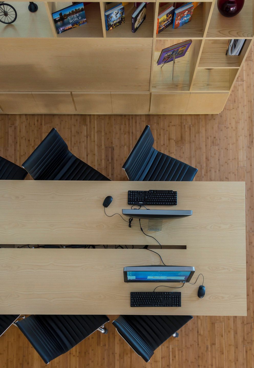 A modern office space with a long wooden table, multiple black chairs, and a bookshelf with travel-themed books.