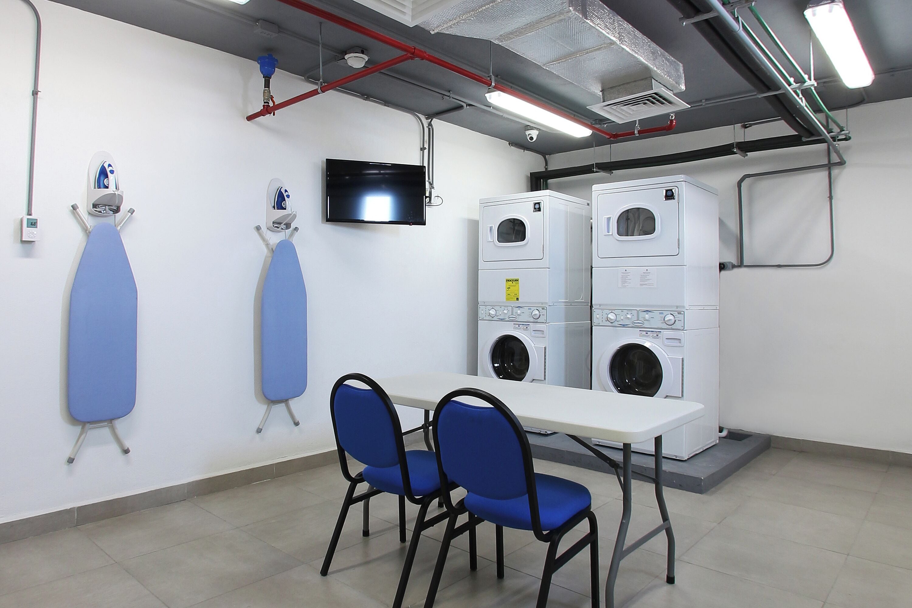 Una habitación con una mesa, dos sillas y dos planchas de ropa fijadas a la pared.