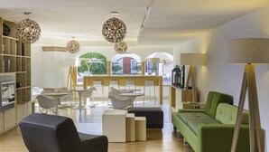 A modern living room with a green sofa, white chairs, a coffee table, and a TV. There are wooden shelves and a floor lamp. - Fiesta Inn Queretaro (Querétaro)