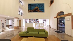 A spacious lobby with a green sofa, wooden tables, and a large painting on the wall. - Fiesta Inn Queretaro (Querétaro)