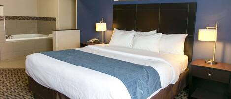 Une chambre d’hôtel avec un grand lit, deux tables de chevet, une petite table, une lampe, un téléphone et une salle de bain avec une baignoire et un lavabo.