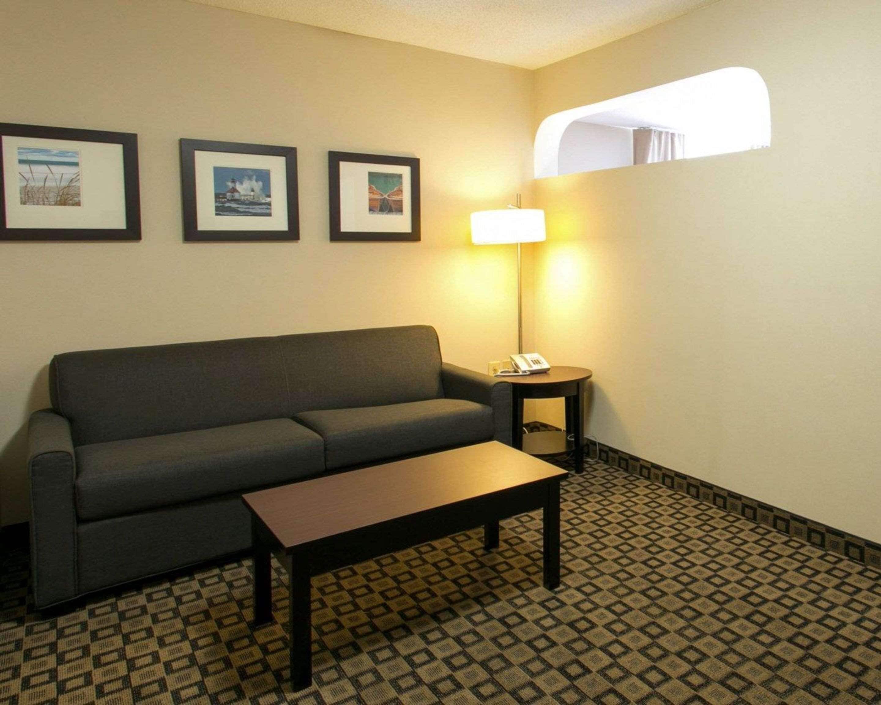 A small, furnished room with a sofa, a table, and a lamp. There are three framed pictures on the wall.