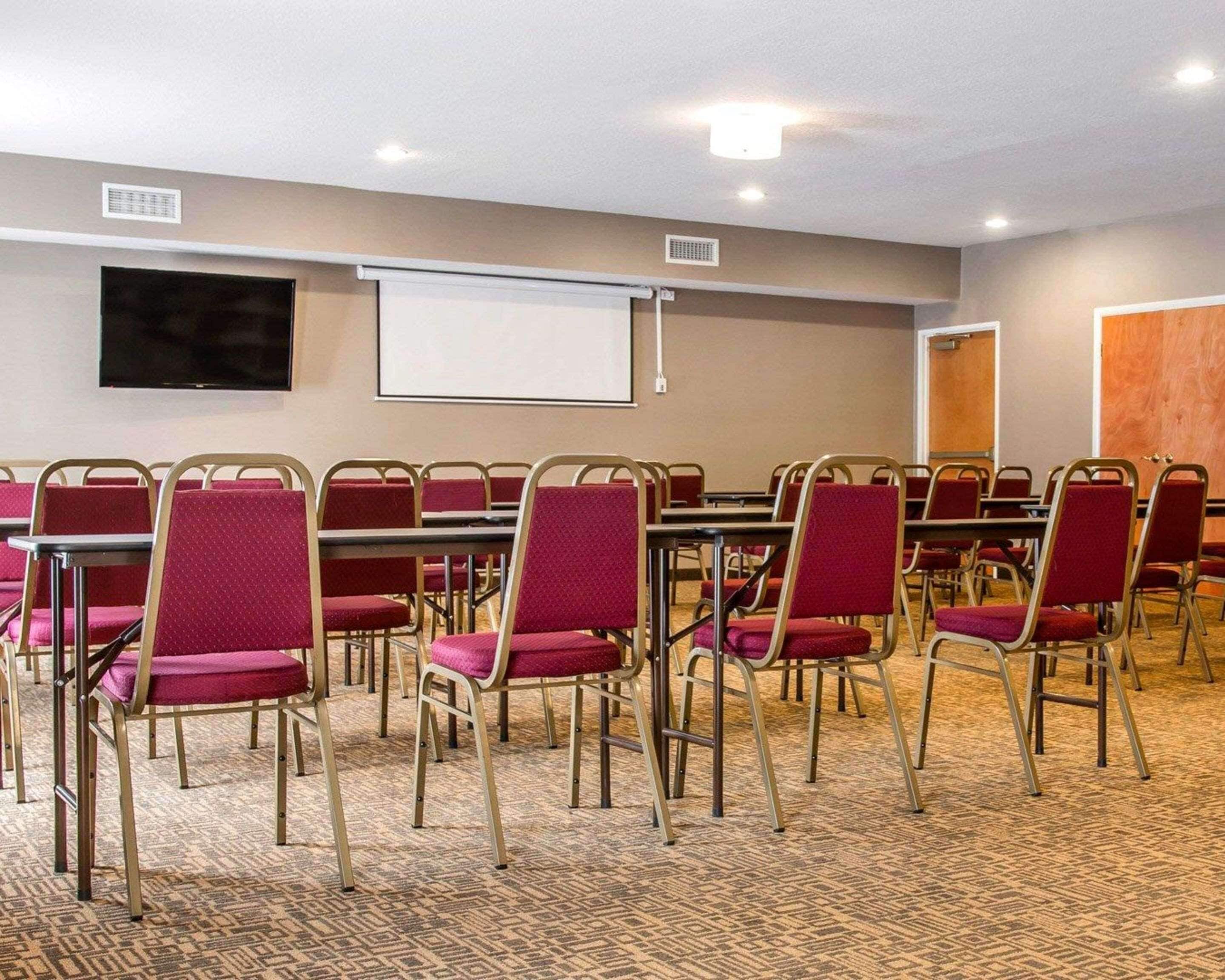 Un salón de conferencias con hileras de sillas rojas, una pantalla de proyector y un televisor de pantalla plana en la pared.