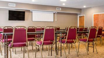 A conference room with rows of red chairs, a projector screen, and a flat-screen TV on the wall.