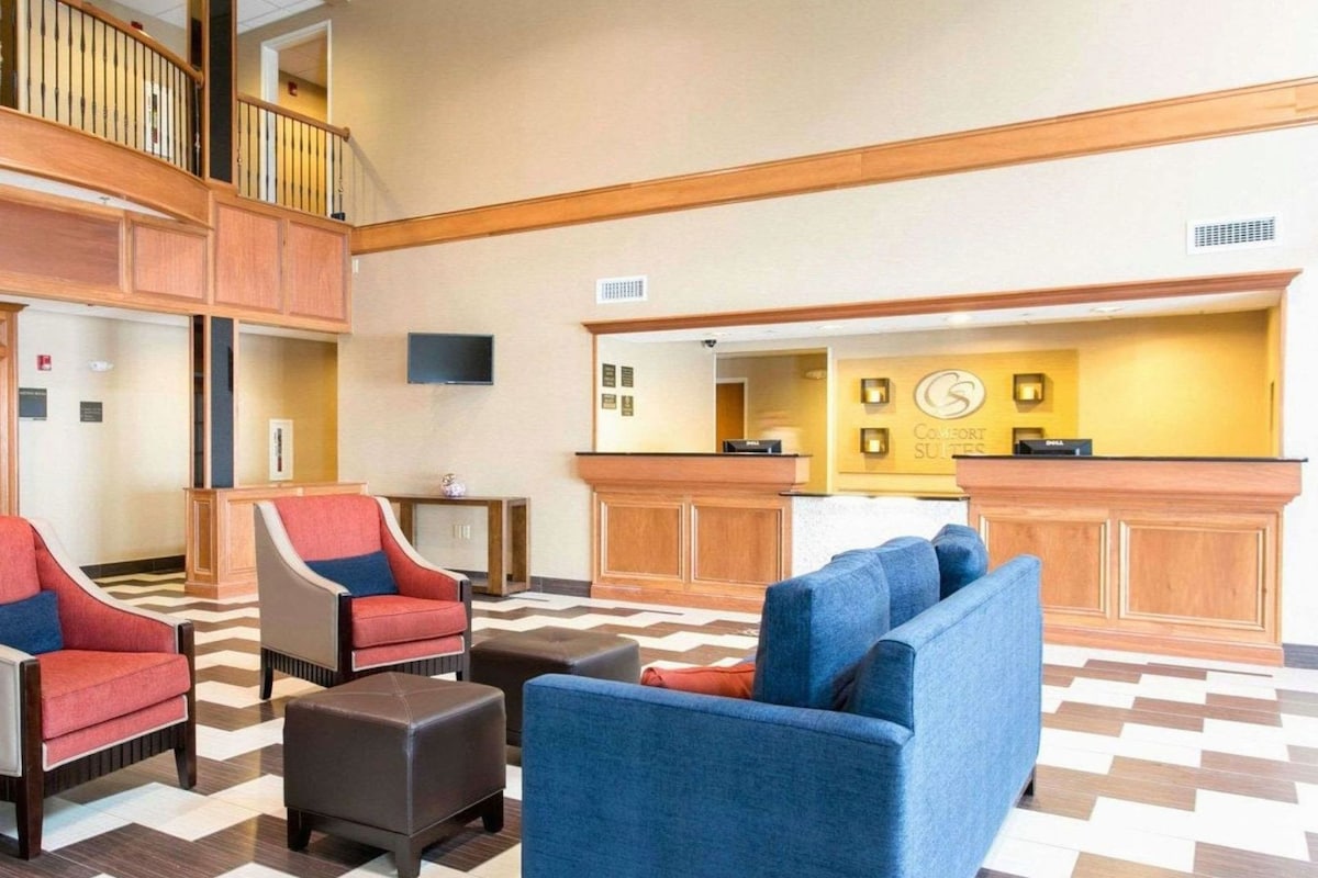 Un hall d’hôtel comprenant un comptoir d’enregistrement, un espace salon avec des fauteuils et des poufs, un téléviseur fixé au mur et un escalier menant à un étage supérieur.