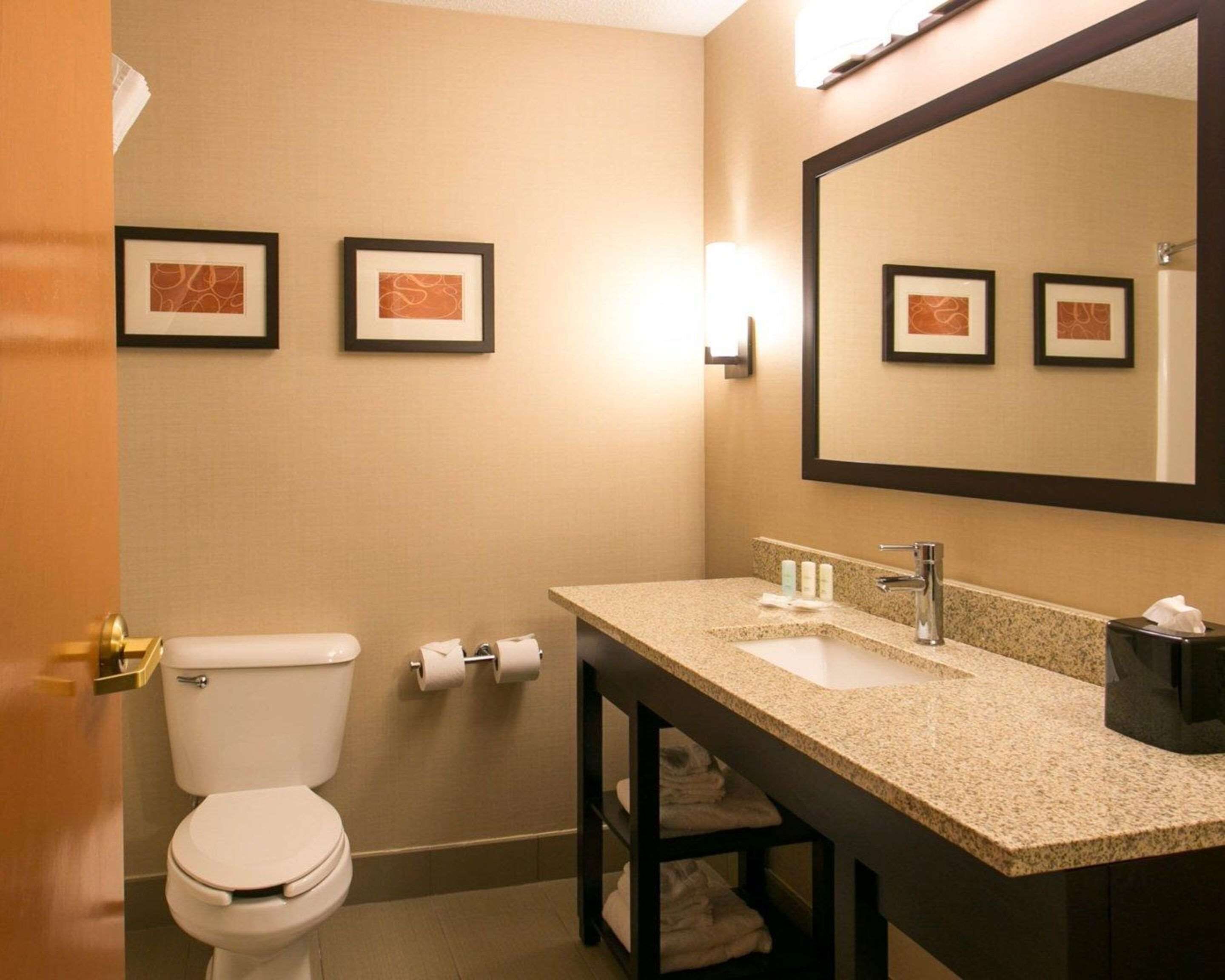 A bathroom with a toilet, sink, and mirror. There are framed pictures on the wall and a towel rack below the sink.