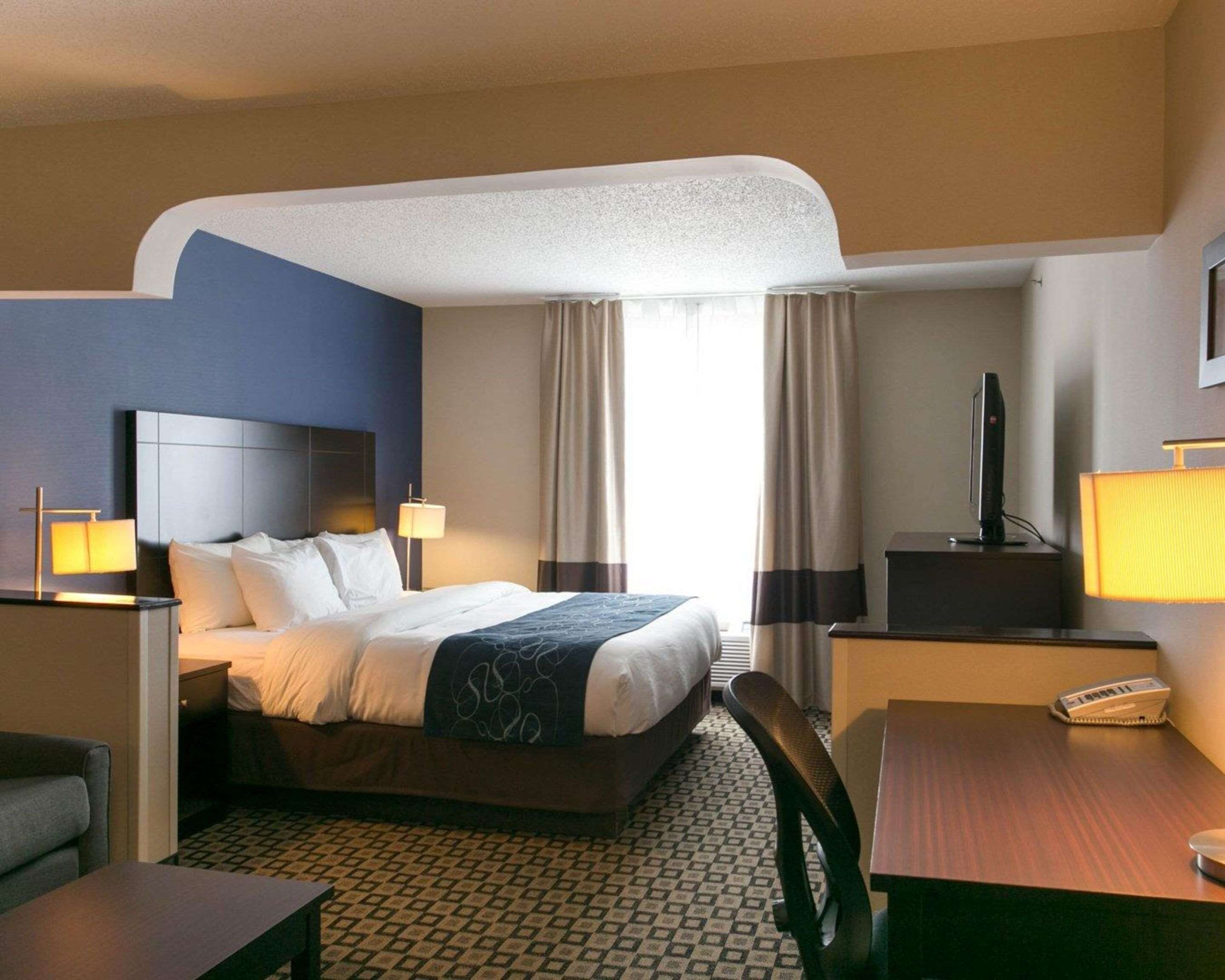 A hotel room with a bed, bedside tables, a desk, a chair, and a television.