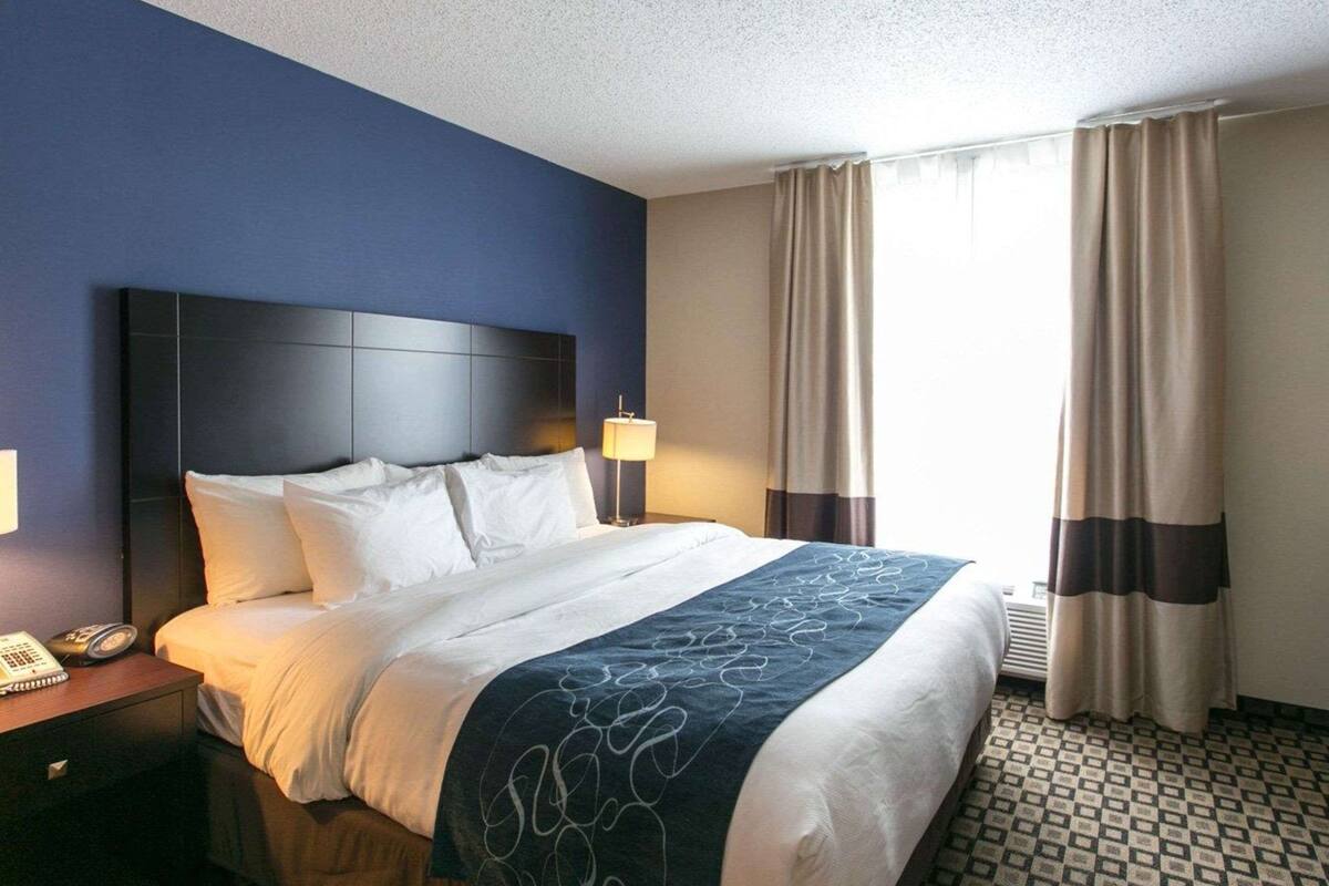 Une chambre d’hôtel avec un grand lit, une table de chevet avec un téléphone et une fenêtre avec des rideaux.