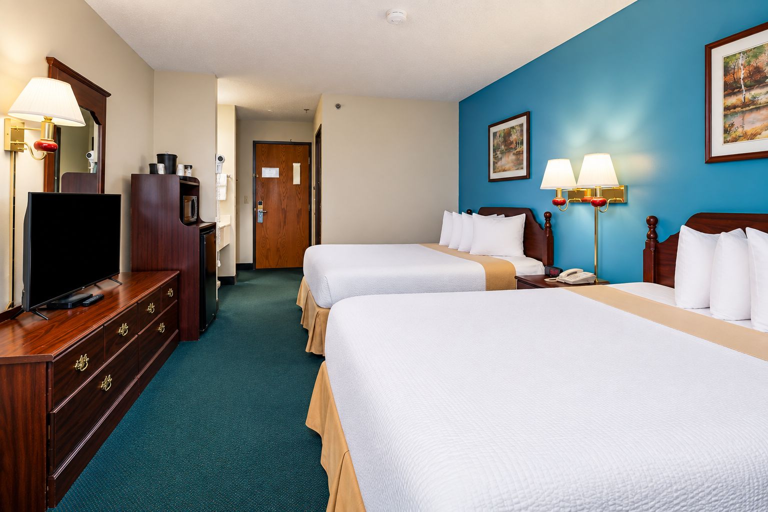 A hotel room with two beds, a TV, a desk with drawers, a lamp, and a painting on the wall.