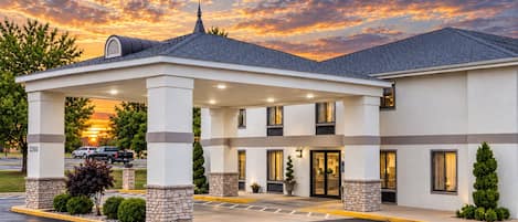 A hotel with a covered entrance, outdoor seating, and a parking area.