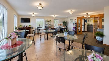 A spacious dining area with multiple round glass tables and chairs, a kitchen area with a dining table, and a living area with a sofa and a coffee table.