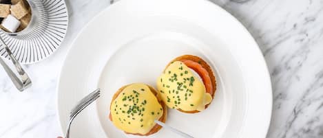 A breakfast setting with two eggs benedict on a white plate, a cup of coffee, and a salt and pepper shaker on a marble surface.