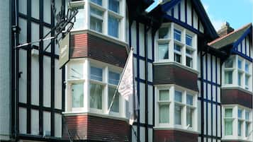 Un edificio tradicional con entrada en esquina, un letrero que dice "Bode" y un asta con una bandera.