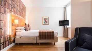 Quarto com uma grande estante de livros, uma cama com manta xadrez, uma televisão e uma poltrona escura.