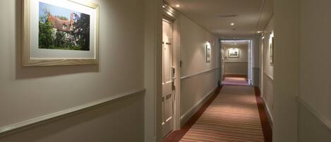 A hallway with a striped carpet, framed pictures on the walls, and doors leading to other rooms.