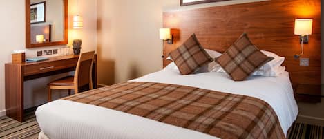 A hotel room with a large bed, a wooden headboard, two bedside lamps, a desk with a chair, and a mirror.