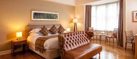 A hotel room with a bed, a brown leather sofa, a small table, and a chair.