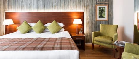Una habitación de hotel con una cama grande, dos lámparas de noche, un sillón verde y un panel de pared de madera.
