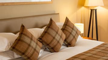A neatly made bed with plaid pillows and a blanket, a bedside lamp, and a window with a view of greenery.