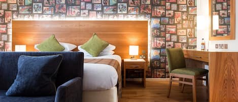 A hotel room with a large bed, two bedside tables, a desk, a chair, and a wall covered with framed pictures.